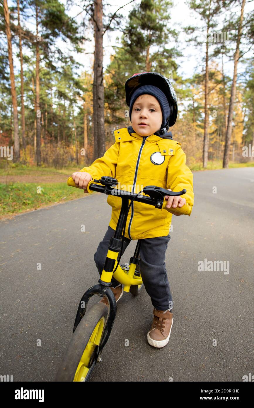 Adorable garçon en tenue décontractée et casque de sécurité debout près de lui equilibrer la moto Banque D'Images