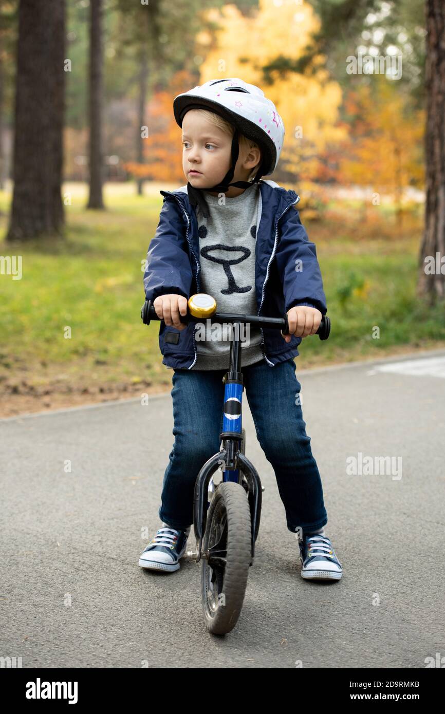Adorable garçon blond en tenue décontractée et casque de sécurité debout route asphaltée Banque D'Images