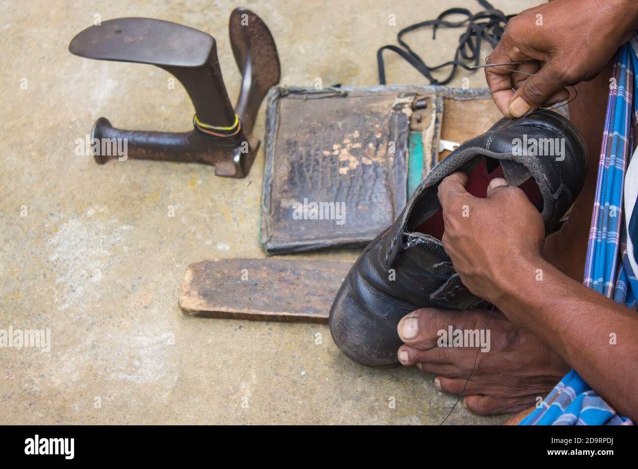 Un cobbler indien local répare les chaussures à côté de la route à la main en utilisant des outils de manière traditionnelle. Photo naturelle illustrant le travail quotidien d'un cobbler ordinaire. Banque D'Images