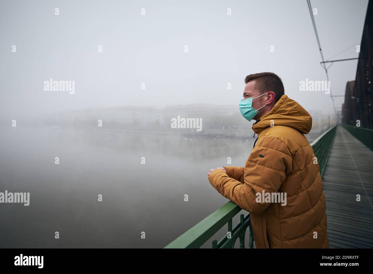 Homme solitaire portant un masque facial sur le pont contre la ville dans le brouillard. Thèmes la vie dans la nouvelle normale, coronavirus et la protection personnelle. Banque D'Images