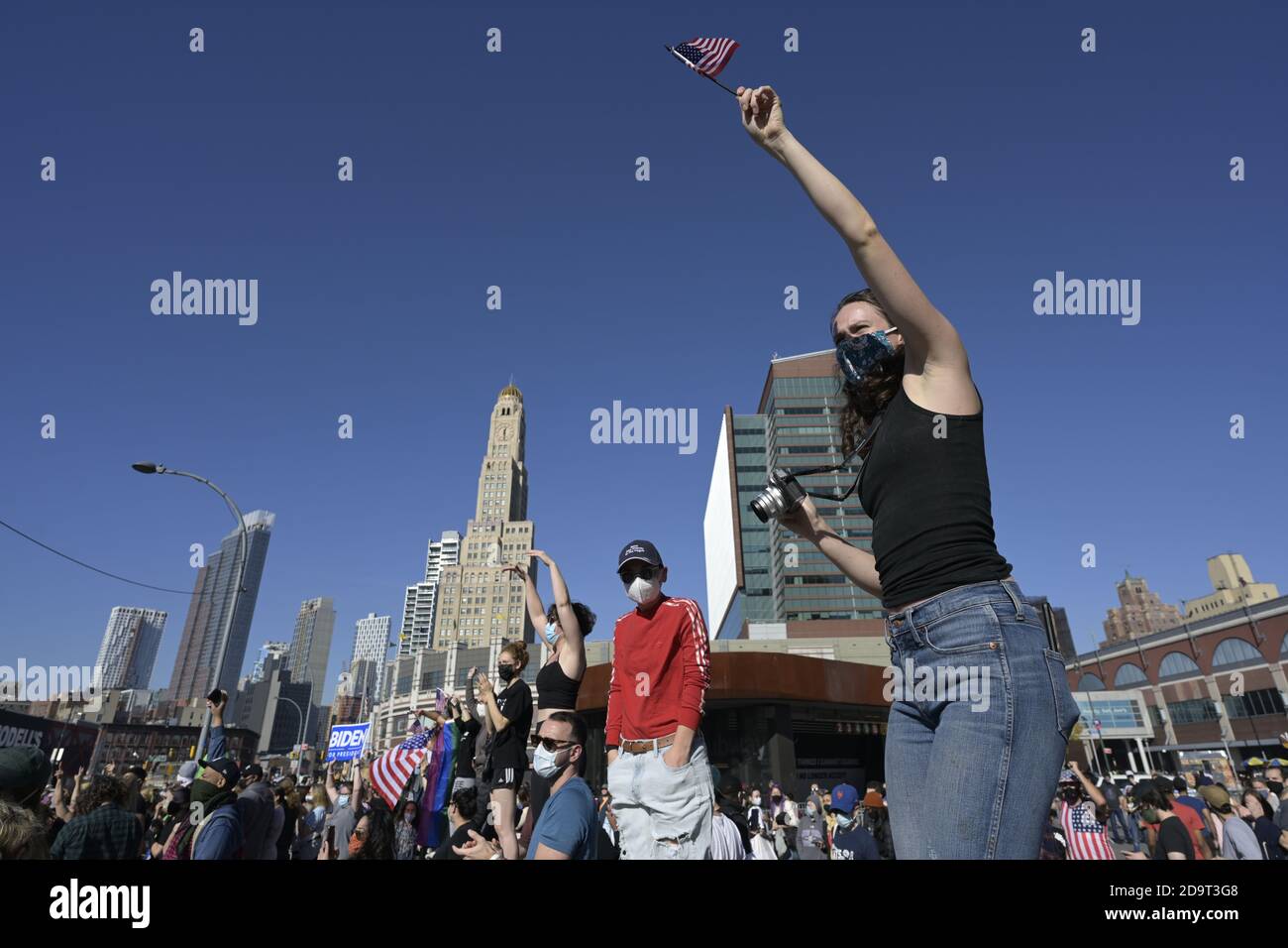 Brooklyn, New York, États-Unis 7 novembre 2020. Une jeune femme debout sur un pylône fait passer un drapeau américain tandis que les gens se rassemblent à l'extérieur du Barclays Center pour célébrer la victoire projetée de Joe Biden dans la course présidentielle américaine Banque D'Images