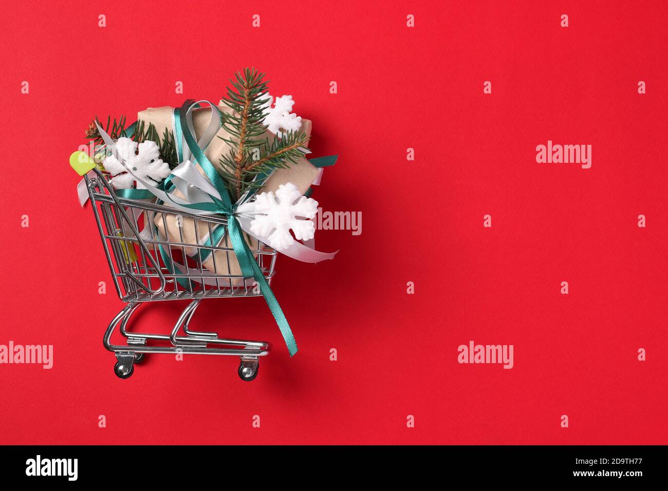Chariot avec cadeaux du nouvel an en papier kraft avec rubans verts et blancs sur la surface rouge. Concept commercial Noël. Espace pour vos souhaits. Carte de vacances Banque D'Images