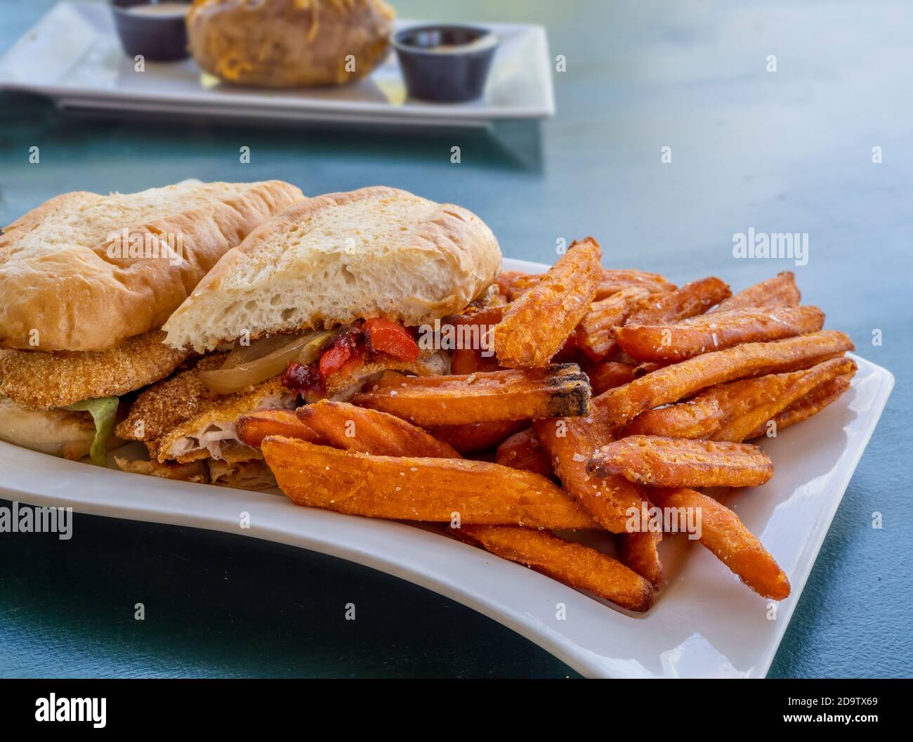 Sandwich au poisson enrobé de semoule de maïs avec frites de patate douce sur un plaque blanche Banque D'Images