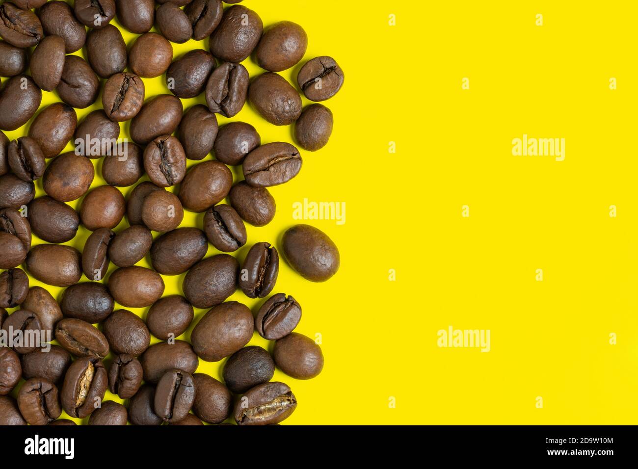 Grains de café noirs sur fond jaune. Objets d'emplacement vertical à gauche, espace de copie pour le texte à droite. Gros plan, plat, couleur du café encore vie. Banque D'Images