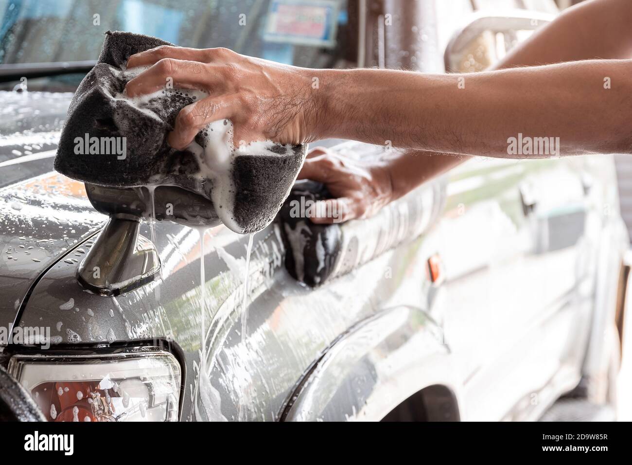 Le personnel de lavage de voiture utilise une éponge humidifiée avec du savon et de l'eau pour nettoyer la voiture. Banque D'Images