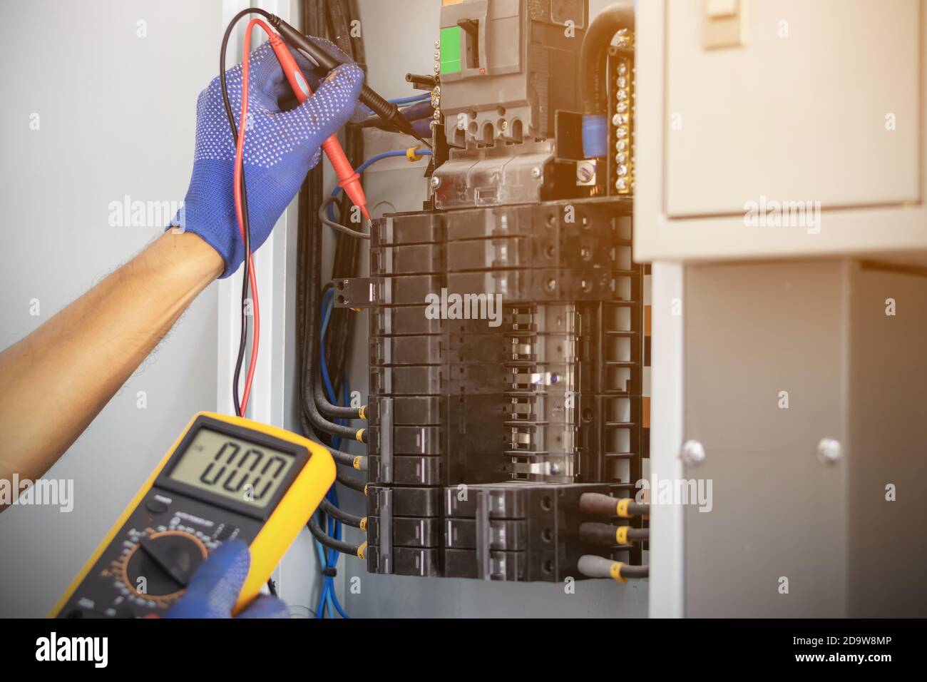 Un électricien utilise un compteur numérique pour mesurer la tension au niveau de l'armoire de commande du disjoncteur sur le mur. Banque D'Images