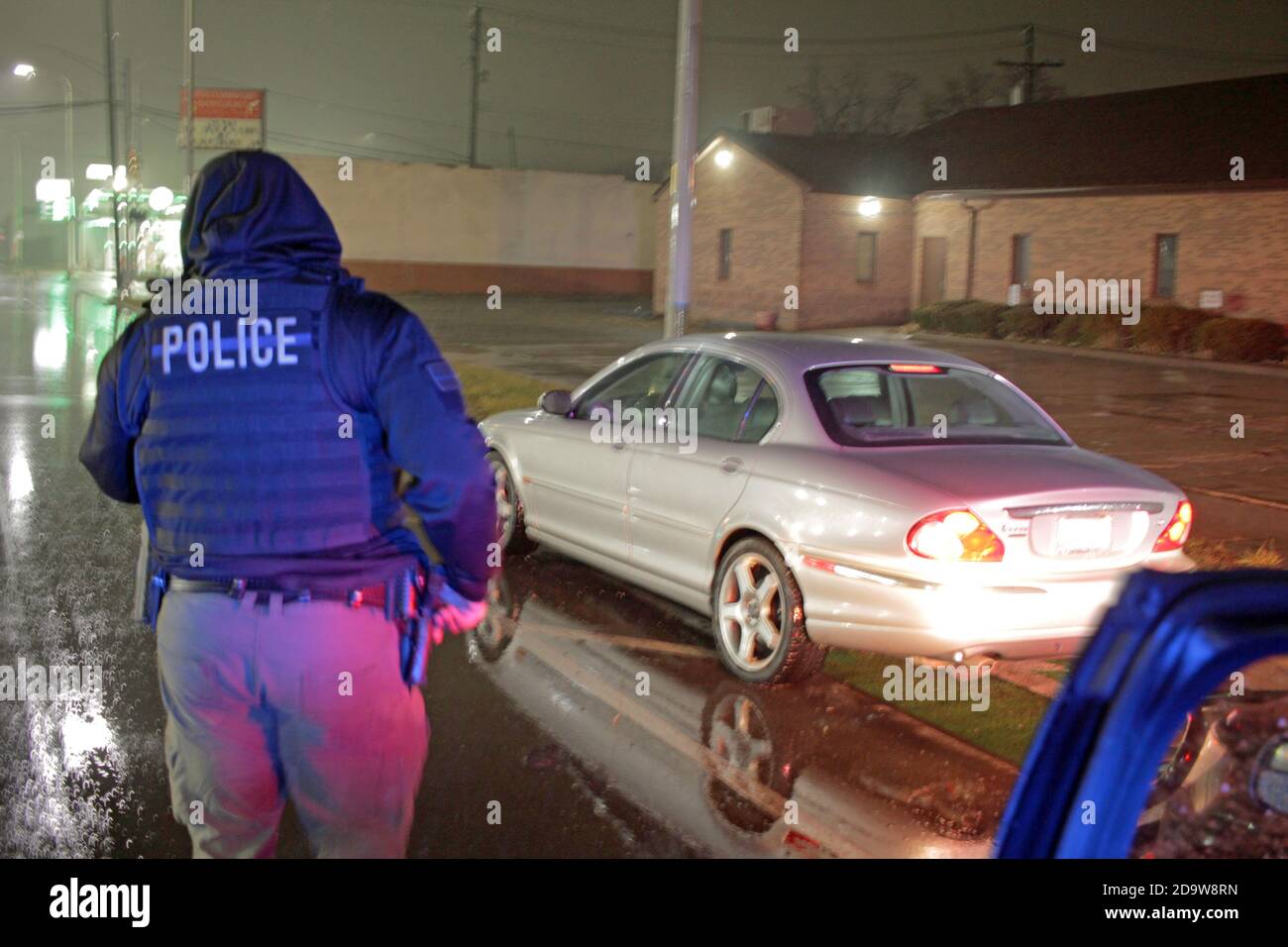 Un agent de police de Detroit évalue une voiture lors d'une nuit de pluie à Detroit, Michigan, États-Unis Banque D'Images