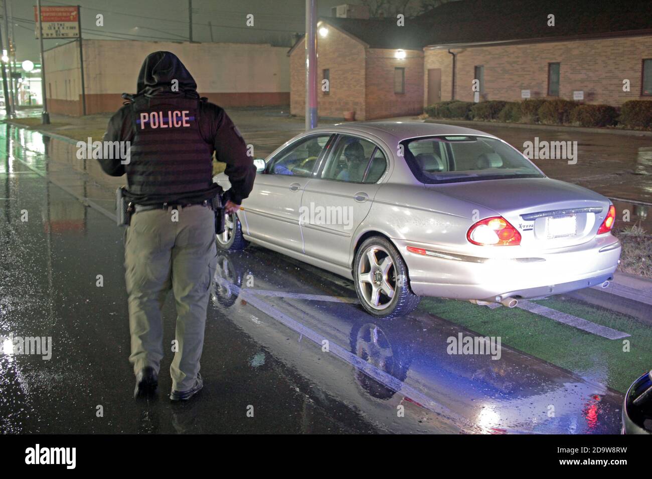 Un agent de police de Detroit évalue une voiture lors d'une nuit de pluie à Detroit, Michigan, États-Unis Banque D'Images