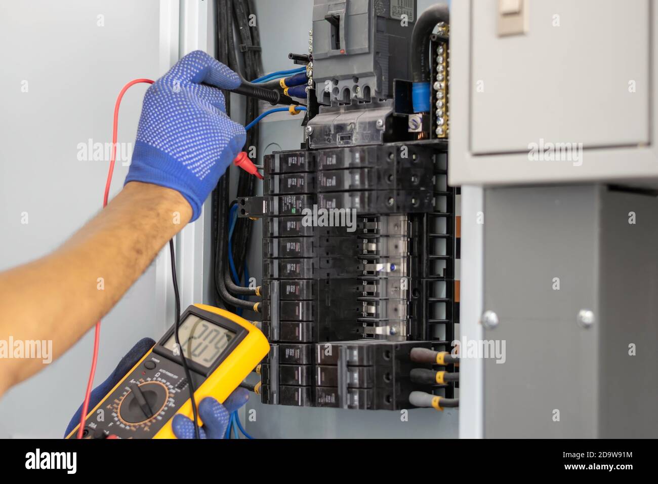 Un électricien utilise un compteur numérique pour mesurer la tension au niveau de l'armoire de commande du disjoncteur sur le mur. Banque D'Images