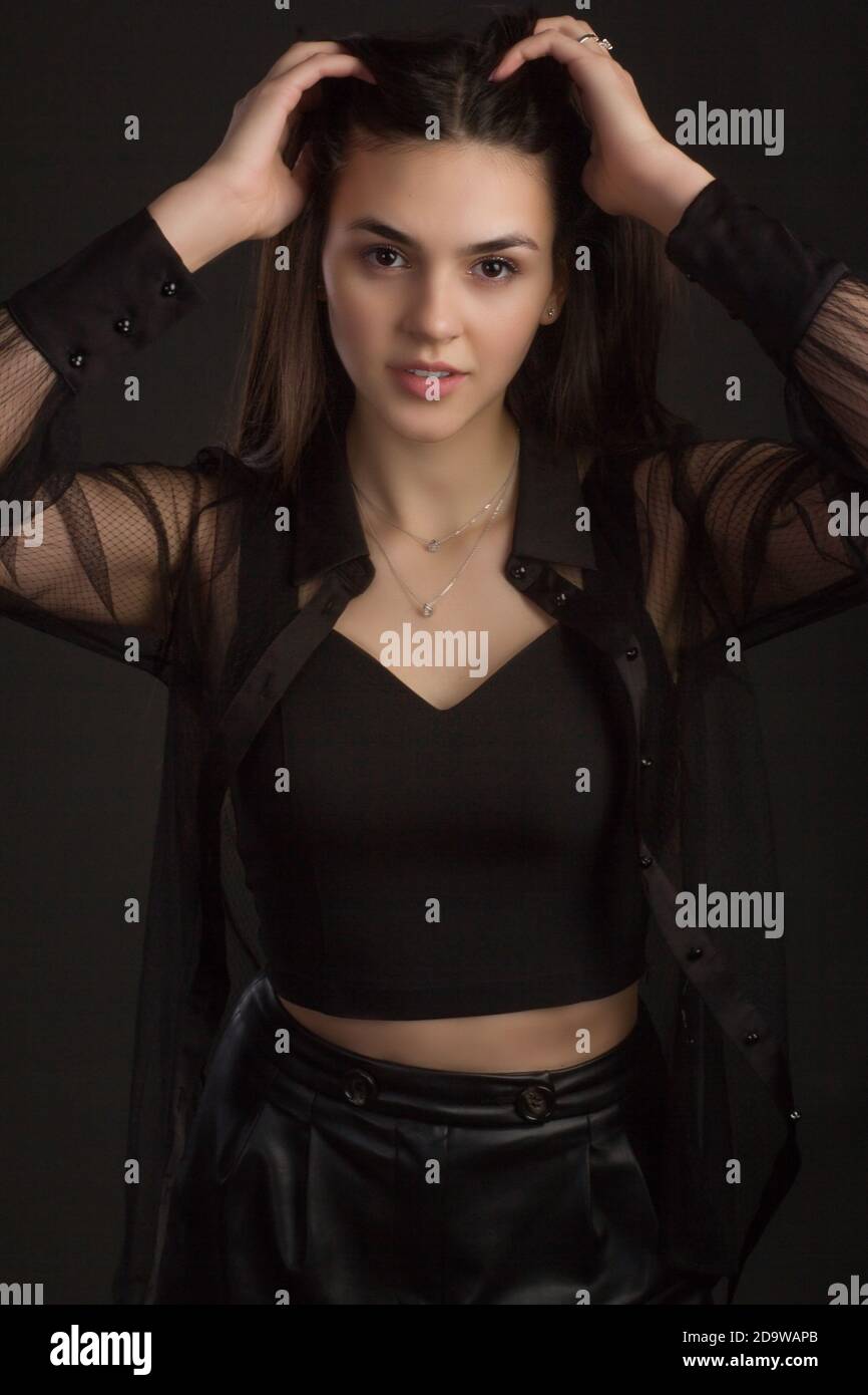 Jeune belle brune avec de longs cheveux, posant dans des vêtements noirs. Dans une photo Studio sur un arrière-plan sombre dans des couleurs chaudes Banque D'Images