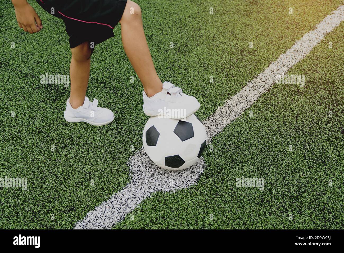 Pieds d'un garçon portant des baskets blanches qui marche sur une balle de football au milieu du terrain de football. Banque D'Images