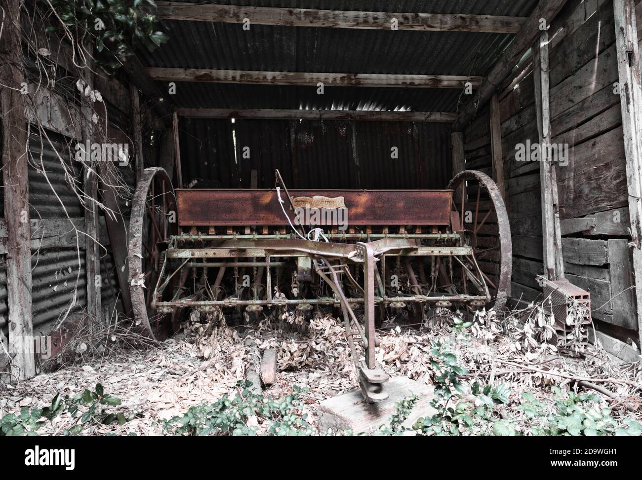 Ancienne graine mécanique abandonnée dans une grange en bois. Métal rouillé. Pneus sans roues. Outil agricole abandonné et abandonné, Banque D'Images