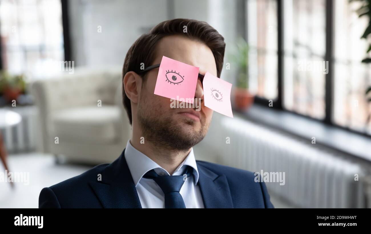 Homme d'affaires épuisé assis au bureau avec des autocollants en papier sur des lunettes. Banque D'Images
