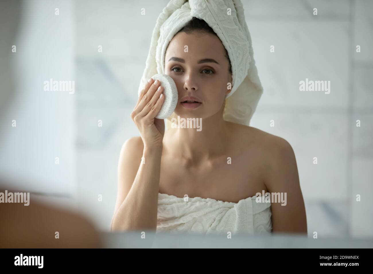 Jeune femme avec une peau délicate sensible essayant une nouvelle éponge pour le visage Banque D'Images