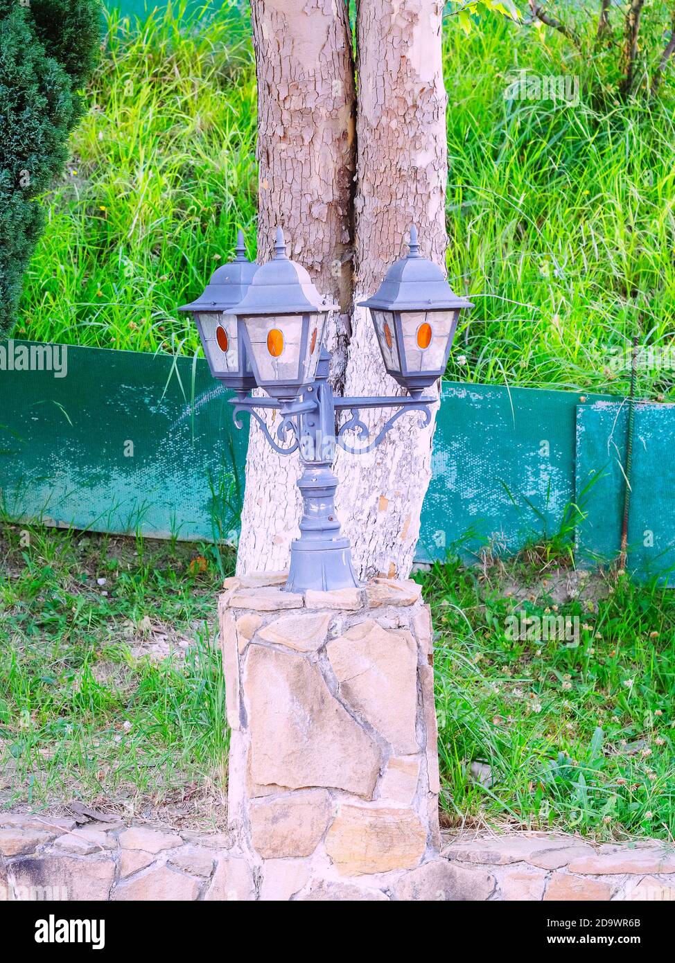 Feu de rue décoratif triple sur un poteau court et un tenez-vous debout avec la maçonnerie contre le fond d'un tronc d'arbre et herbe verte Banque D'Images