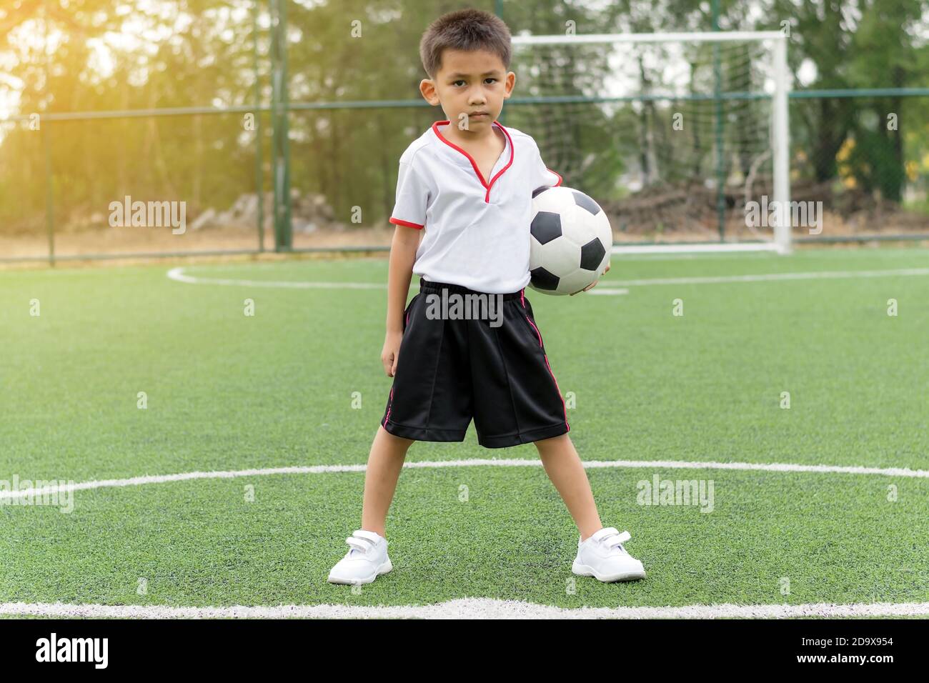 Un garçon asiatique tient un ballon de football sur le terrain. Banque D'Images