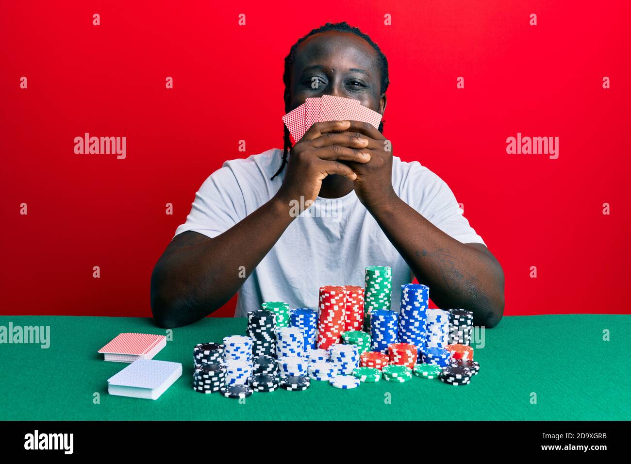 Beau jeune homme noir jouant au poker de jeu couvrant le visage avec des cartes souriant avec un sourire heureux et cool sur le visage. Montrant des dents. Banque D'Images