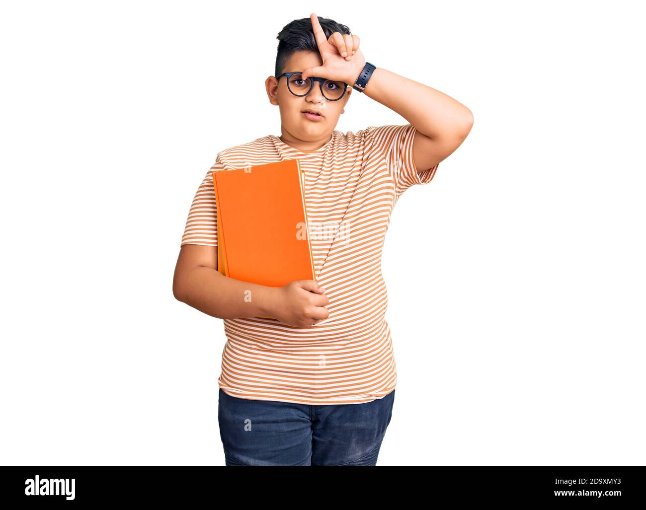 Petit garçon enfant tenant le livre portant des lunettes rendant amusant de personnes avec les doigts sur le front faisant le geste perdant mocking et insultant. Banque D'Images