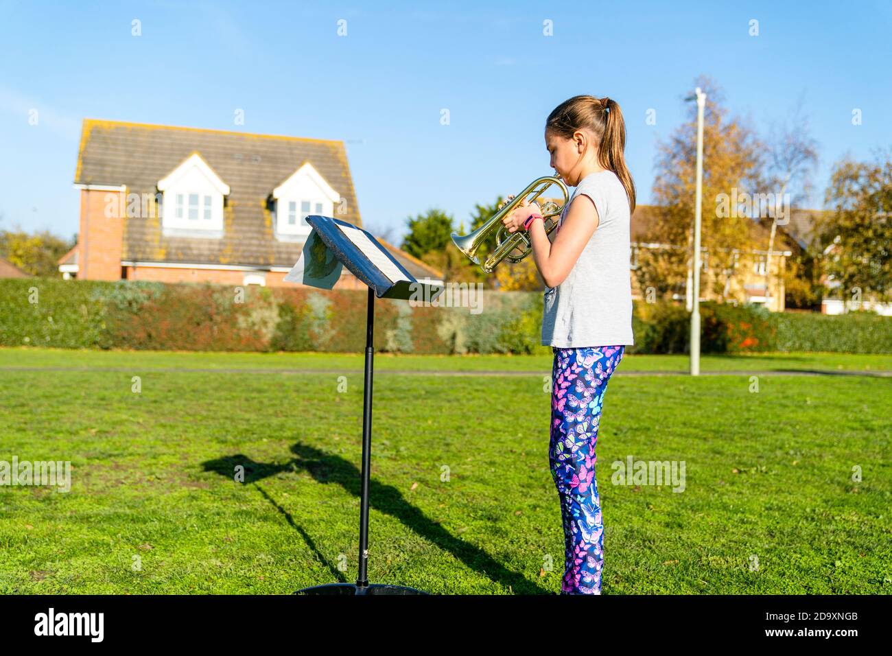 Enfant caucasien, fille, femme, 9-10 ans, debout devant un stand de musique tout en jouant la trompette, à l'extérieur sur le village vert avec des logements en arrière-plan, l'hiver. Ciel bleu clair au-dessus de la tête. L'événement jouait le « dernier post » le dimanche du souvenir au Royaume-Uni. Banque D'Images