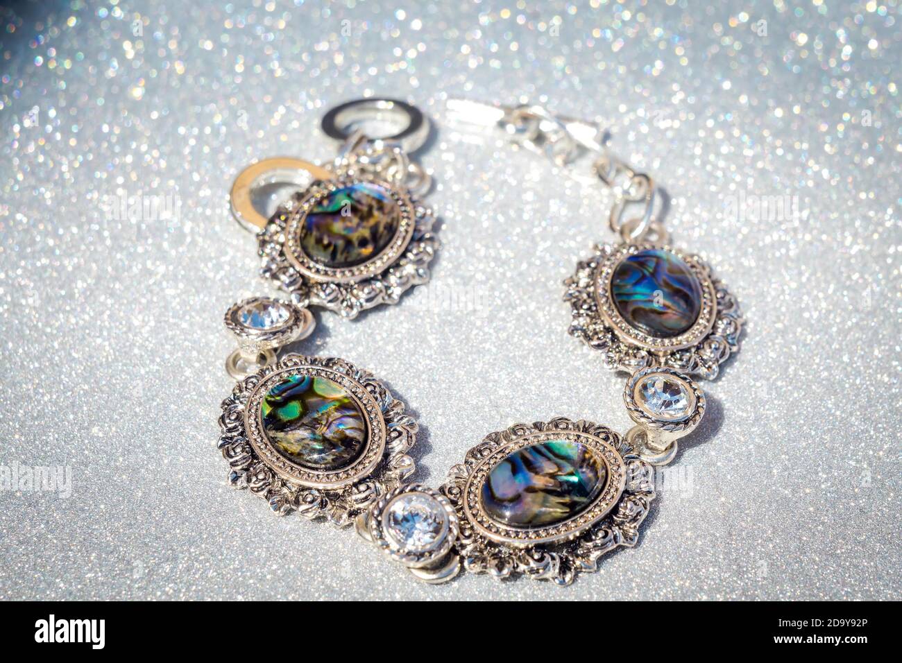Bracelet argent rétro de mode décoré de coquillages d'ormeau arc-en-ciel foncé sur fond de paillettes. Banque D'Images