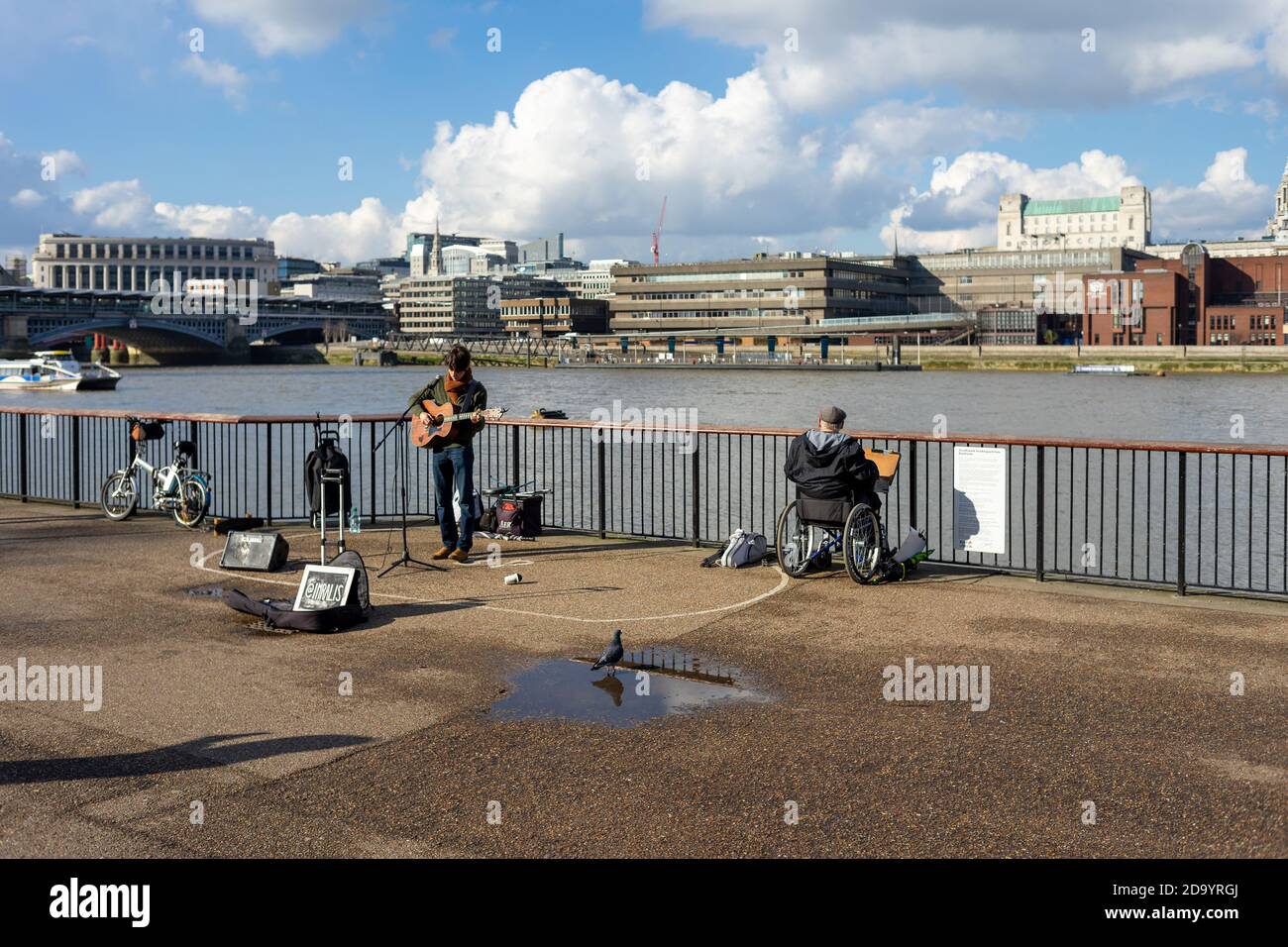 Un interprète de rue se produit à l'extérieur de Tate Modern à Bankside, Londres, tandis qu'une personne handicapée surplombe la Tamise Banque D'Images