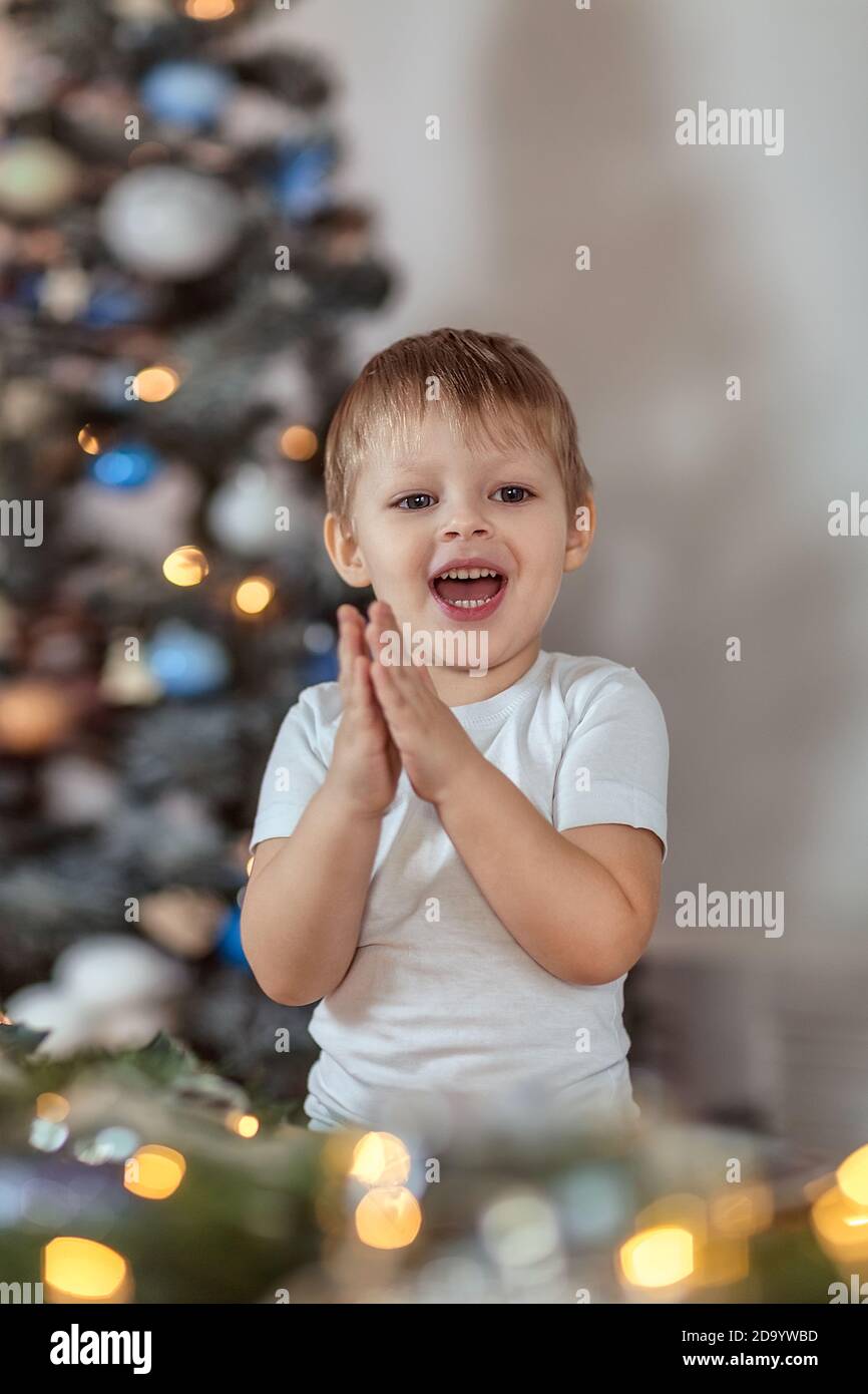 Un beau garçon de 4-5 ans est assis ou debout près de l'arbre de Noël. Il rêve de vacances et de cadeaux, fait un vœu. Le concept du wi Banque D'Images