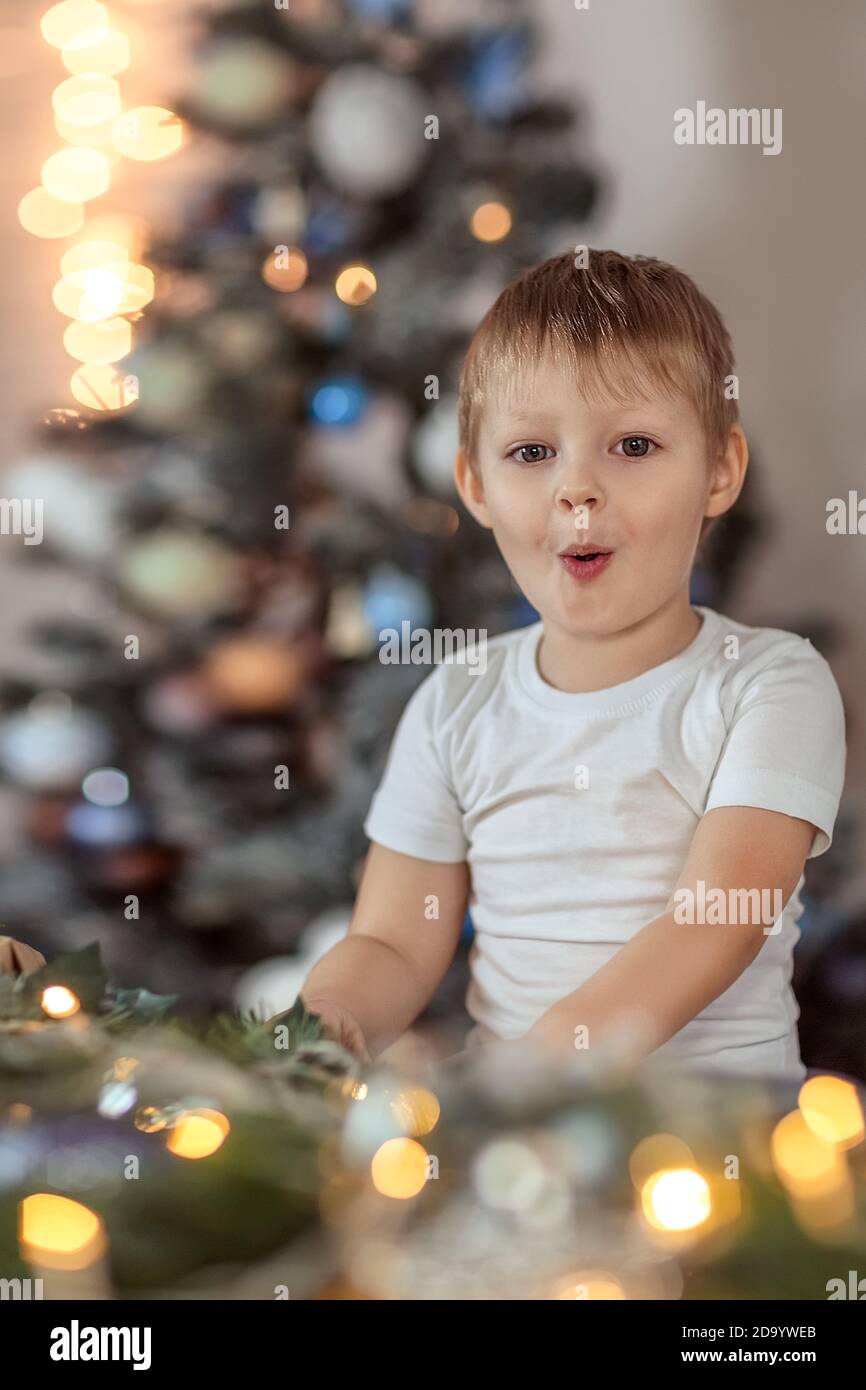 Un beau garçon de 4-5 ans est assis ou debout près de l'arbre de Noël. Il rêve de vacances et de cadeaux, fait un vœu. Le concept du wi Banque D'Images