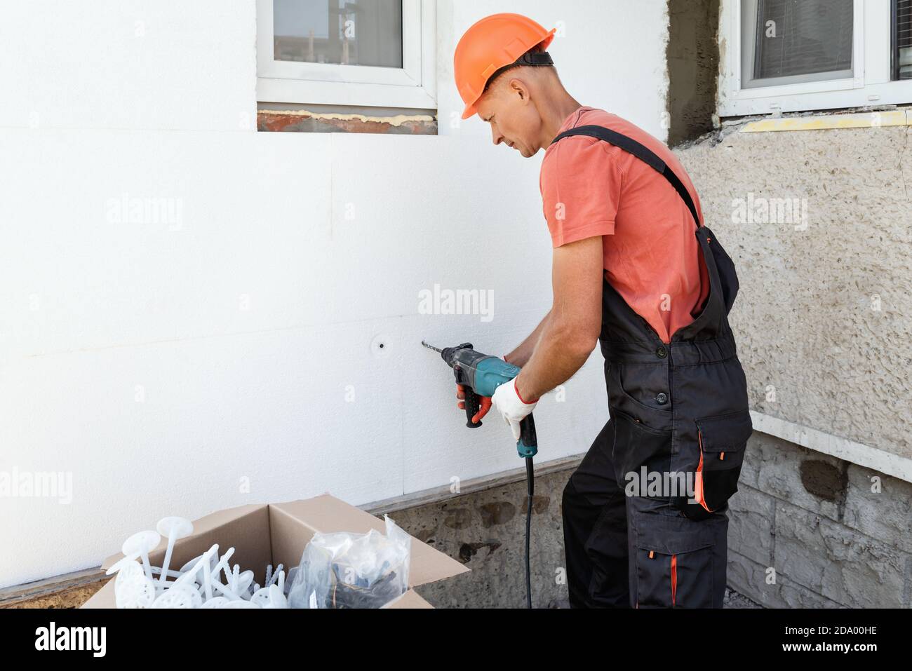 Isolation de la maison avec polymousse. L'ouvrier forer des trous pour fixer le panneau de mousse de polystyrène sur la façade. Banque D'Images