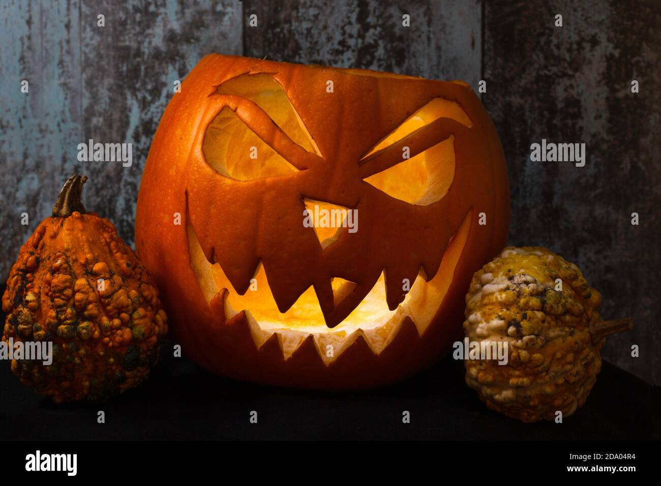 Citrouille sculptée Jack O'Lantern avec visage diabolique et citrouilles miniatures Sur un fond de bois - la tradition d'Halloween Banque D'Images