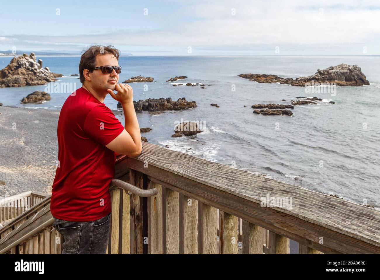 Un jeune homme se trouve sur la terrasse d'observation en bois de Cobble Beach, sous le phare de Yaquina Head à Newport, Oregon Banque D'Images