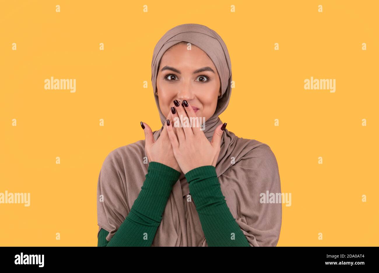 Musulmane Dame dans hijab couvrant la bouche avec les mains, fond jaune Banque D'Images