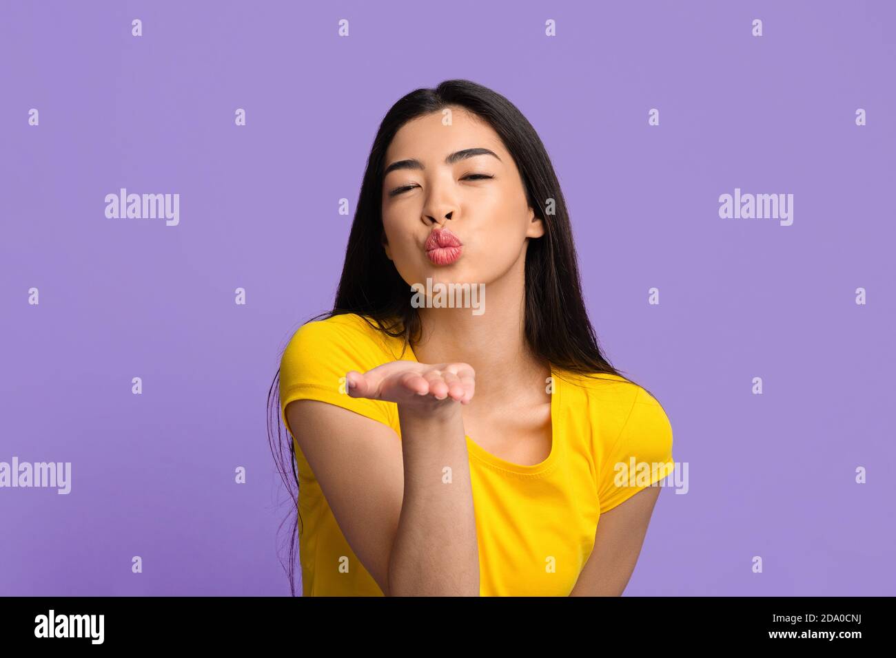 Mignonne jeune femme asiatique soufflant de l'air Kiss à la caméra plus Fond violet Banque D'Images