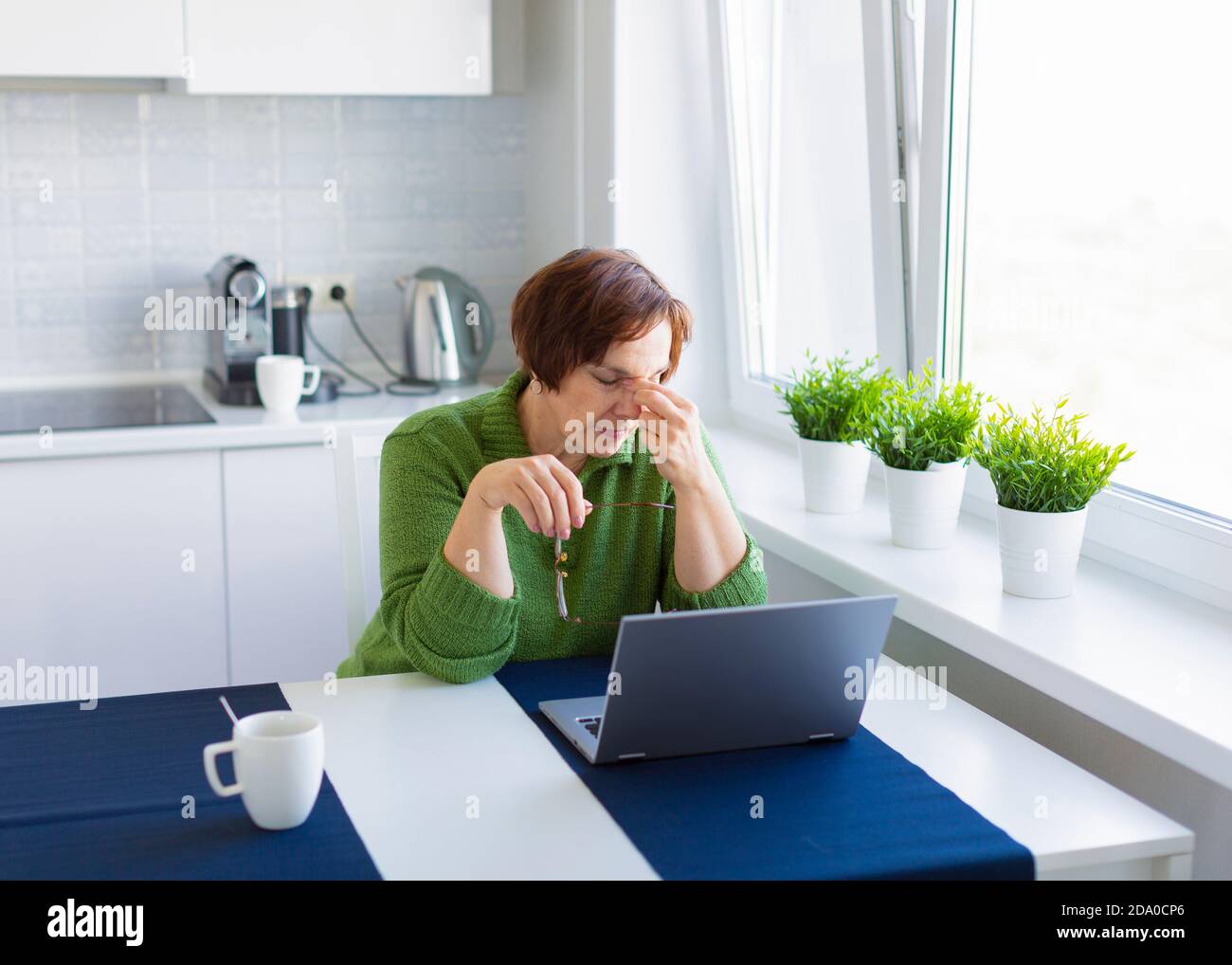 Une femme de 60 ans fatiguée devant un moniteur maque le pont de son nez. Banque D'Images