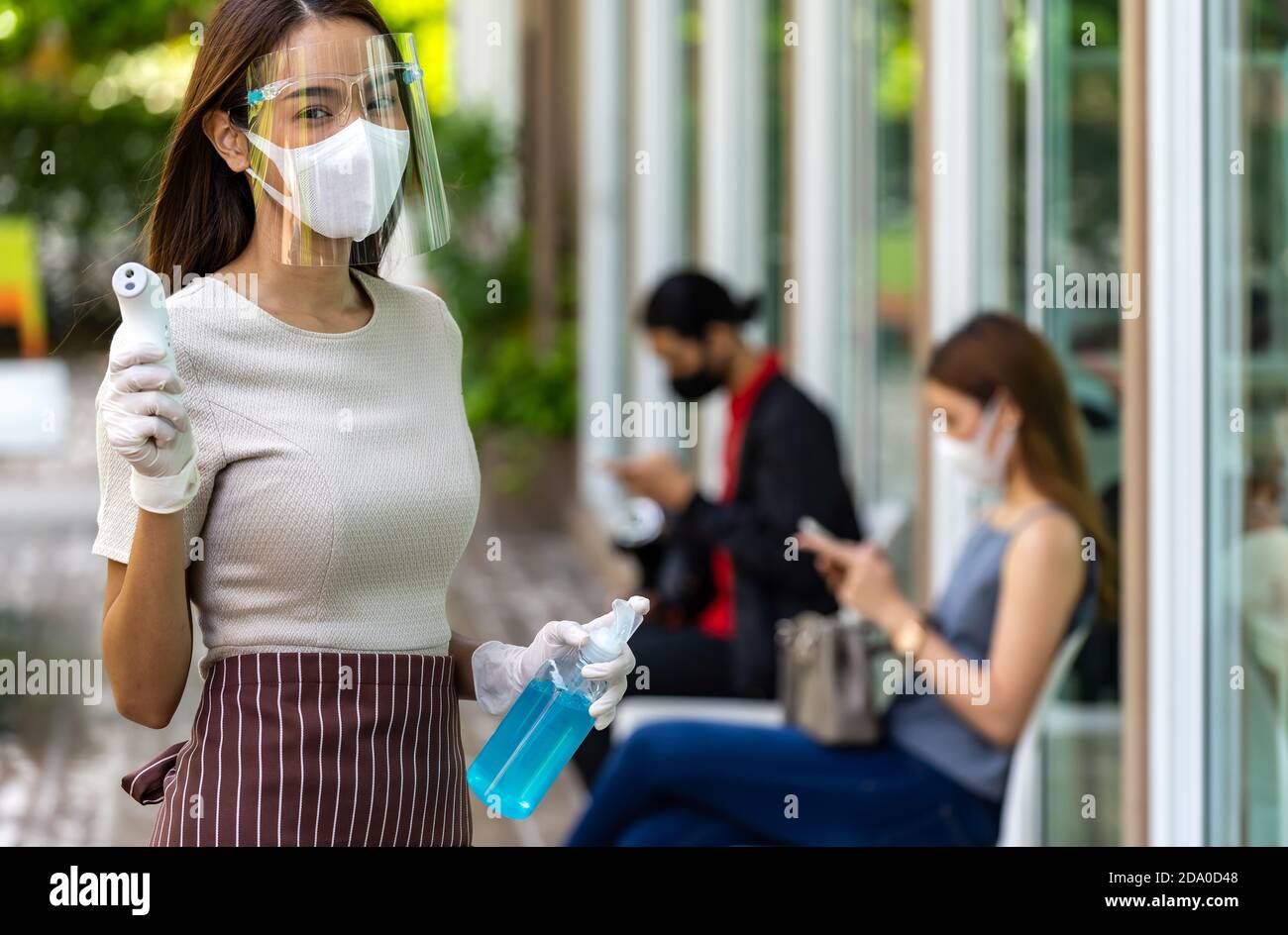 Portrait attrayant serveuse asiatique porter un masque facial et un thermomètre avec protection et gel désinfectant à base d'alcool avec fond de client de distanciation sociale Banque D'Images