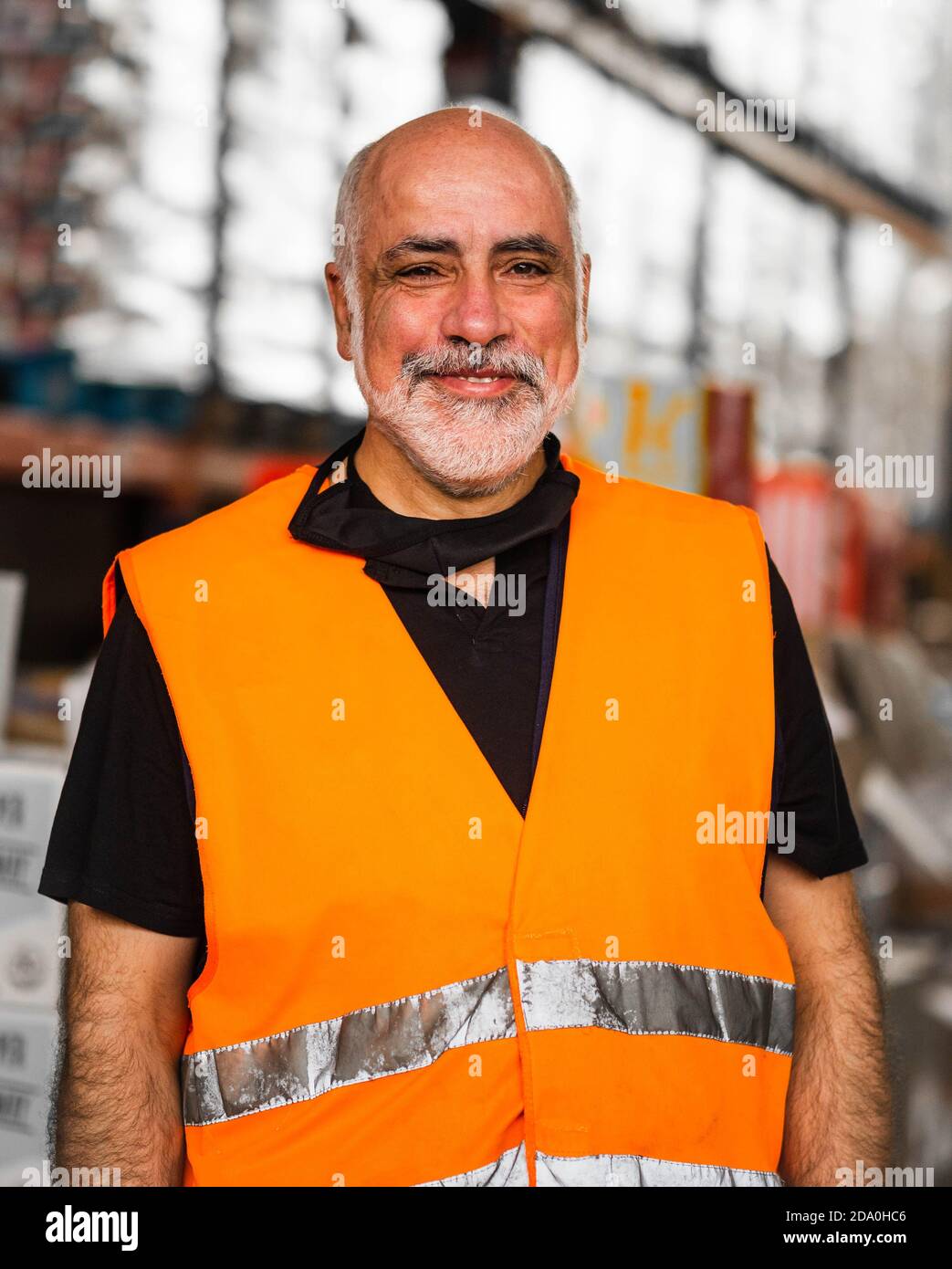 Homme adulte sérieux portant un gilet orange haute visibilité debout près  des racks de l'entrepôt et en regardant la caméra Photo Stock - Alamy