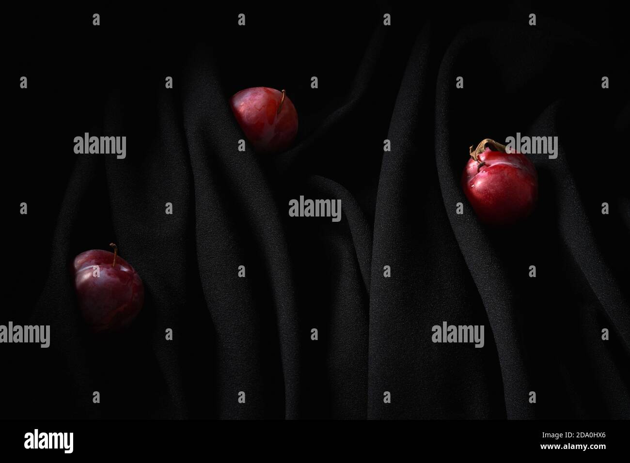 Petites cerises rouges sur les tiges minces placées sur le noir foncé chiffon froissé en studio Banque D'Images