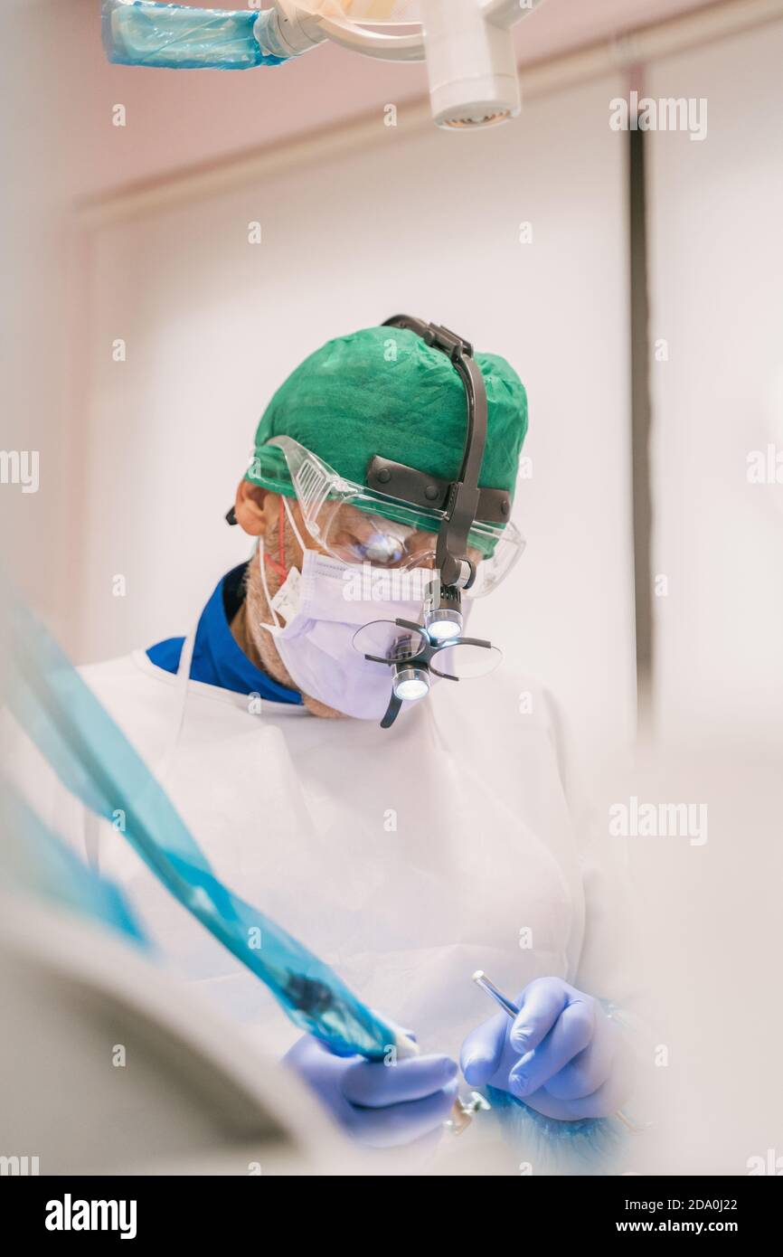 Orthodontiste mâle non reconnaissable dans le masque et les lunettes de protection travaillant à proximité équipement médical en clinique Banque D'Images