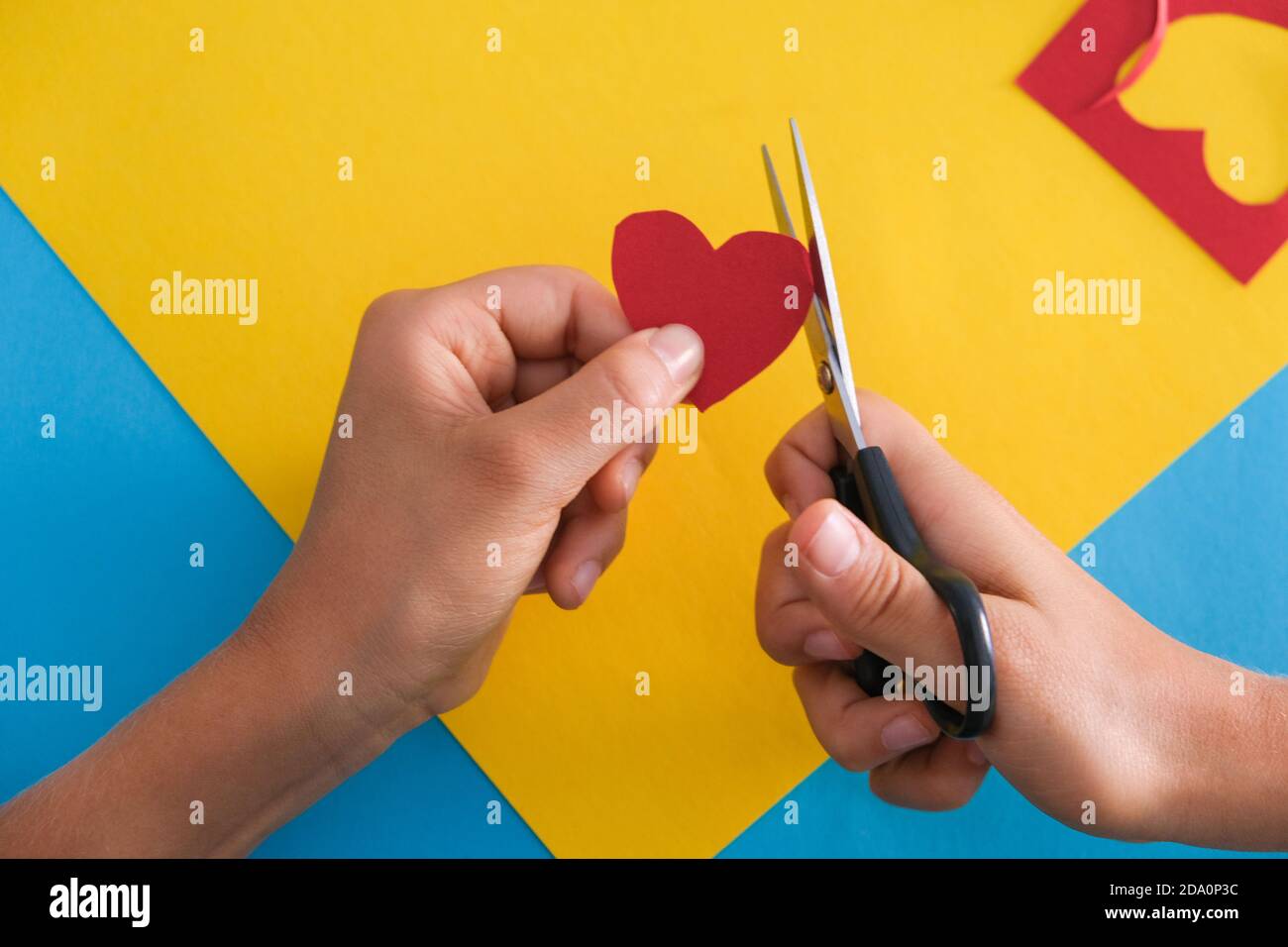 Artisanat en papier pour les enfants. Les mains des enfants coupantes du papier de couleur avec des ciseaux à la table. Vue de dessus Banque D'Images