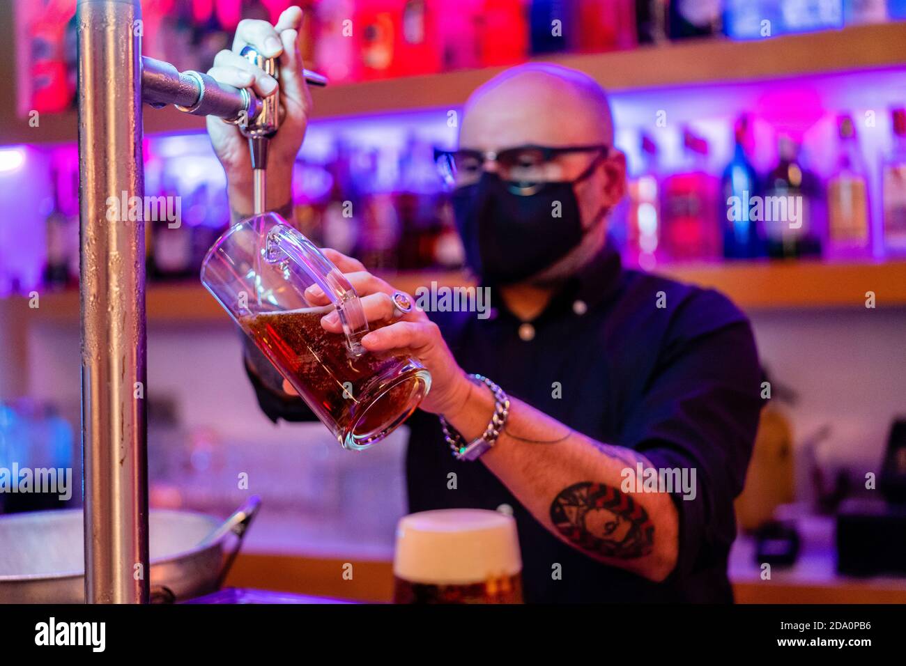Vue latérale d'un barkeeper sérieux dans des lunettes de vue qui versent de la bière verre pendant qu'il travaille en bar pendant une pandémie de coronavirus Banque D'Images