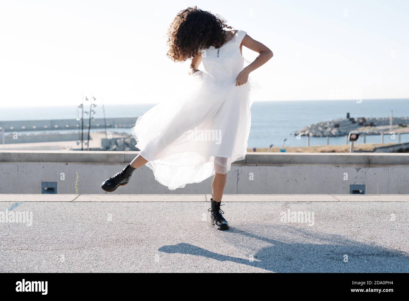 Femme rebelle méconnue dans une élégante robe blanche et des bottes  brutales dansant au soleil sur le toit Photo Stock - Alamy