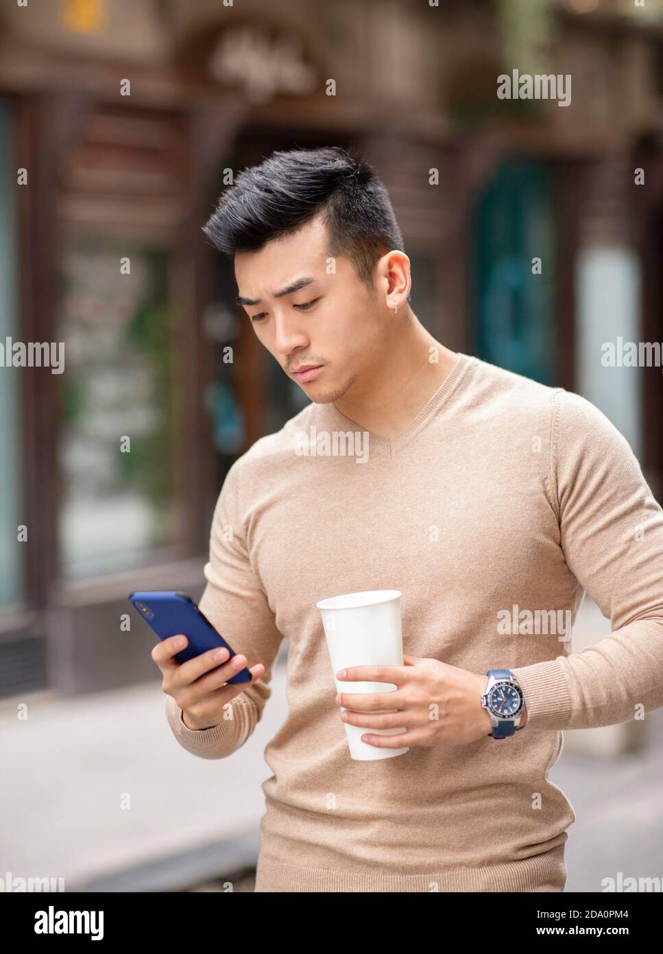 Homme asiatique debout dans la rue avec boisson chaude aromatique à lire des messages sur les réseaux sociaux via un téléphone portable Banque D'Images
