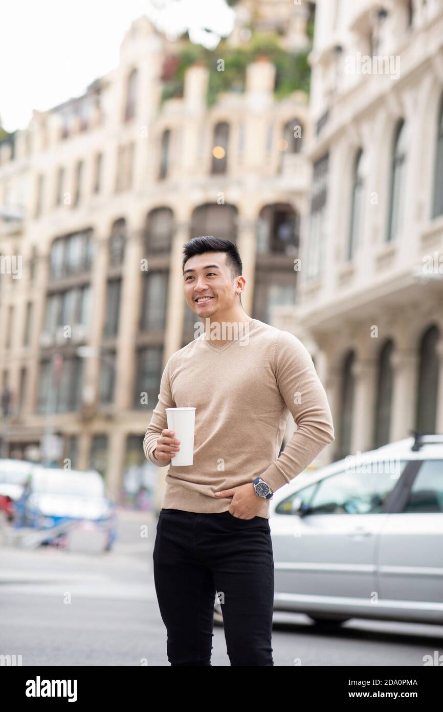 Homme asiatique gai debout près du bâtiment avec un cocktail sucré à profitez d'un week-end en ville tout en admirant la vue Banque D'Images