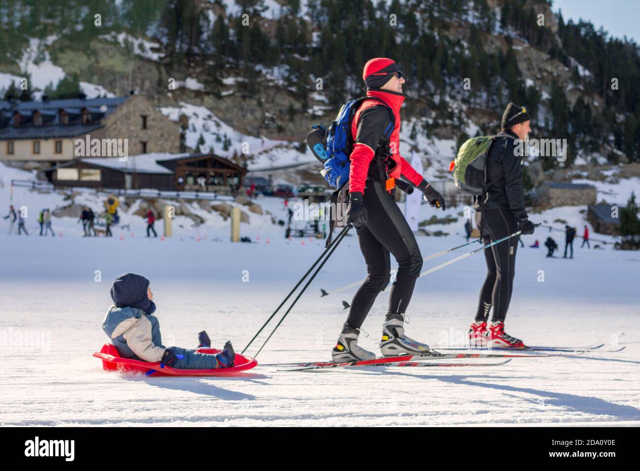 Père et ami pratiquant le ski nordique et fils pratiquant un traîneau dans une station de ski. Banque D'Images