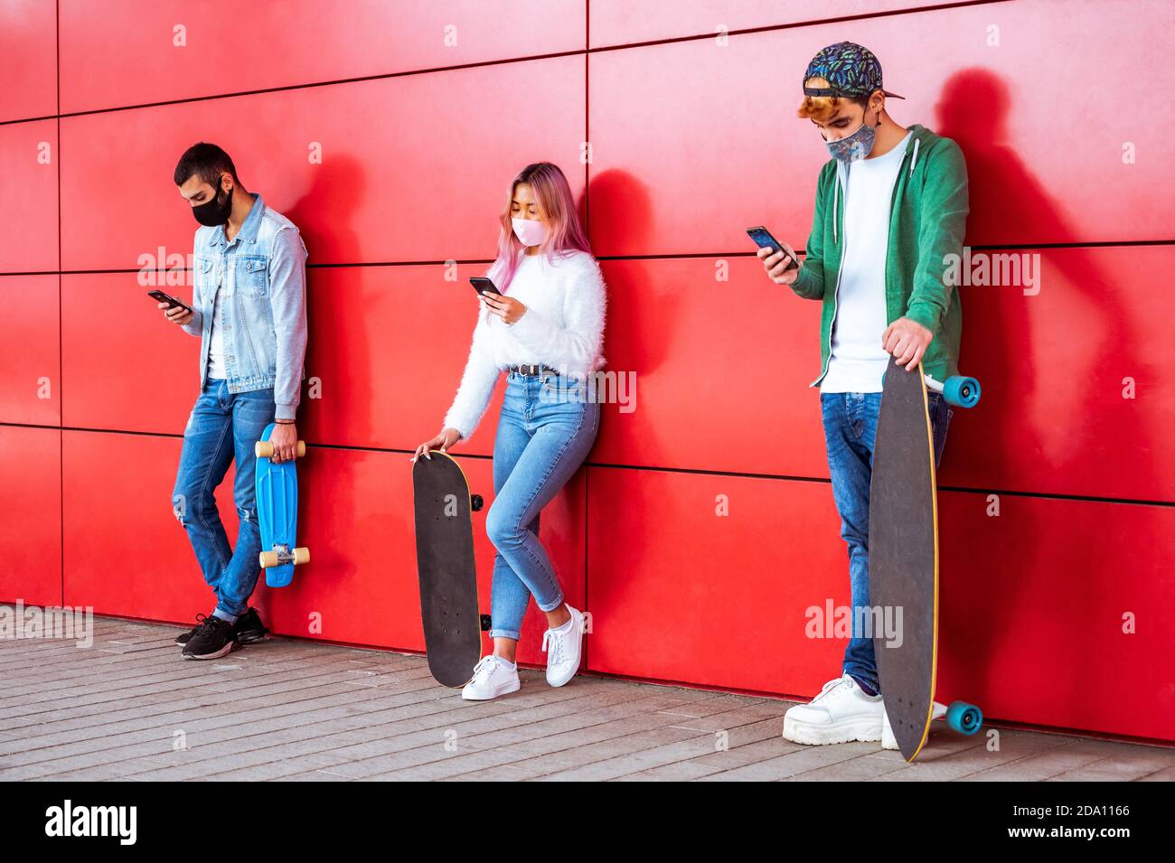 Adolescents avec masque pour le visage messages texte de téléphone mobile s'appuyant sur Mur urbain dans la distanciation sociale - Groupe d'amis multiraciaux utilisation du cellulaire Banque D'Images