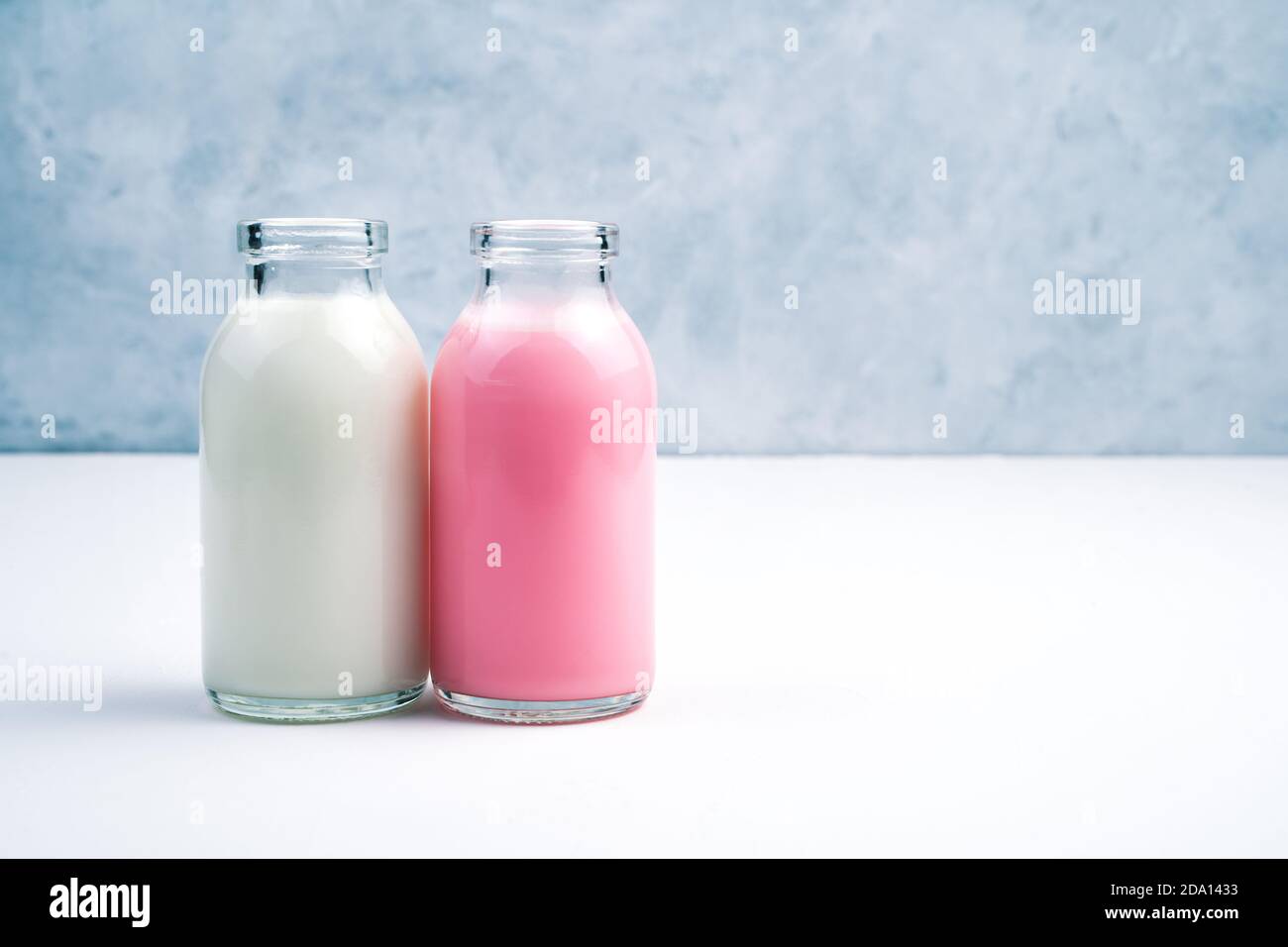 Milk-shakes roses et blancs en flacons sur fond blanc et gris. Banque D'Images