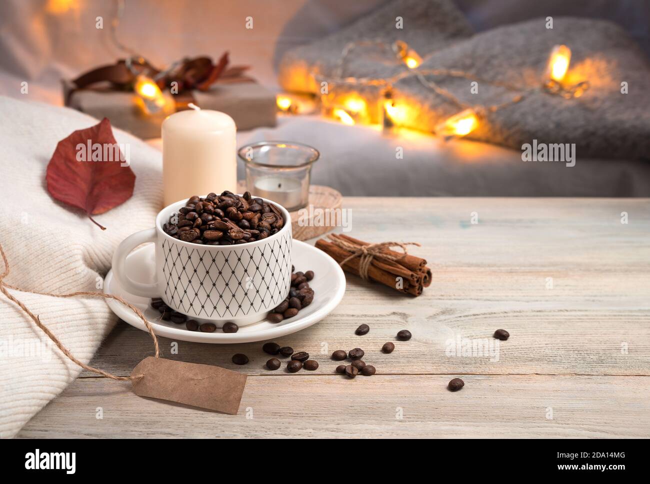Fond de café du soir avec grains de café entiers dans une tasse, bougie et pull sur fond de lumières allumées. Banque D'Images