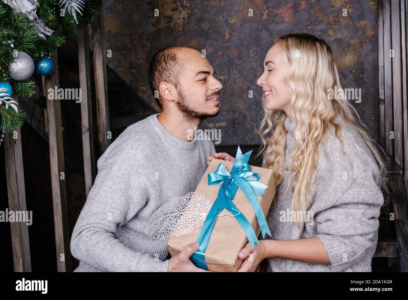 Le jeune couple aimant échange des cadeaux pour la nouvelle année. Le mari embrasse sa femme et donne un cadeau pour la nouvelle année. Cadeau de Noël et du nouvel an à la maison. Banque D'Images