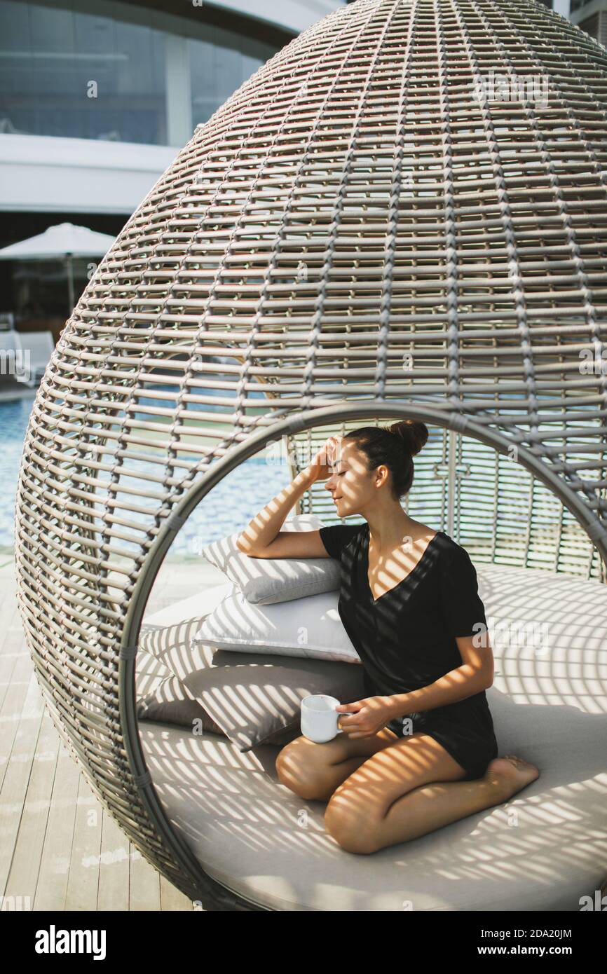 Jeune femme asiatique se détendant et buvant du café dans un lit extérieur  en forme de cocon. En rotin. Décoration contemporaine de mobilier d' extérieur Photo Stock - Alamy