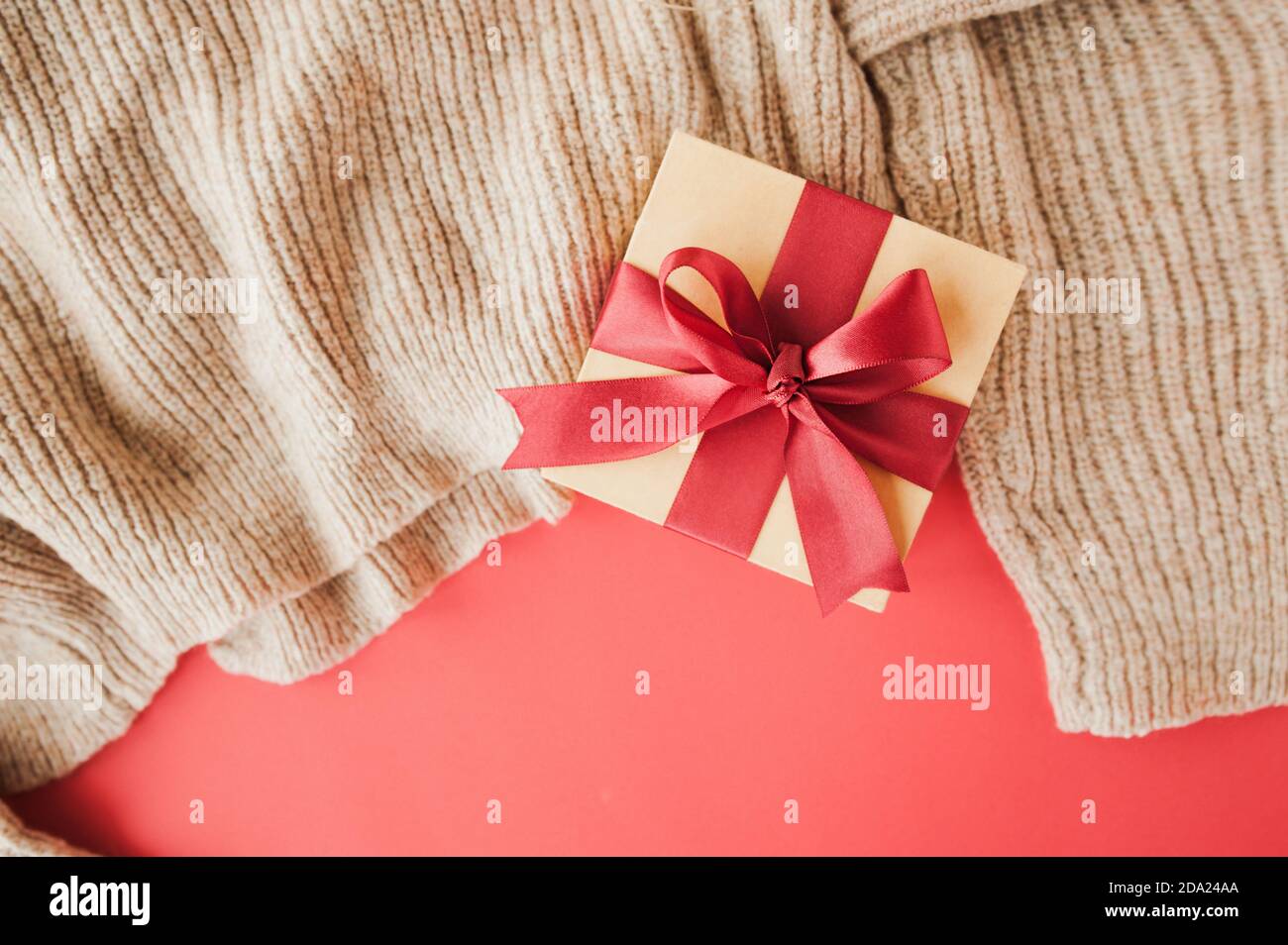 boîte beige avec ruban rouge satiné festif sur chandail beige. présentation des cadeaux, mise au point sélective Banque D'Images