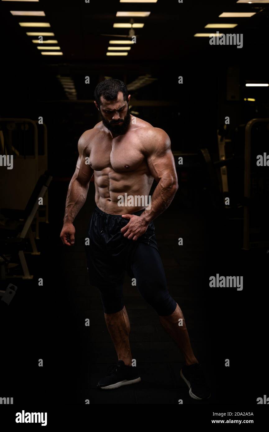 jeune athlète fort, homme barbu avec corps physique sportif parfait dans la salle de sport de nuit posant Banque D'Images